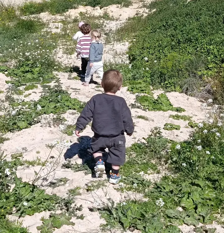 Tres peques caminan de espaldas por un sendero entre flores